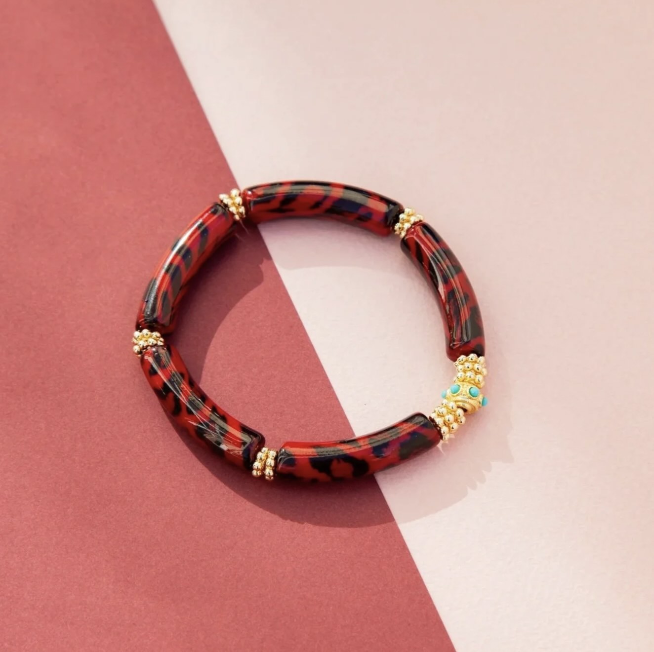 Red and black patterned bracelet with gold accents on a two-tone pink background